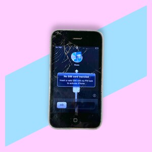 May include: A black iPhone with a cracked screen displays a message: "No SIM card installed." The phone is set against a pink and blue geometric background. The screen shows the iTunes icon.