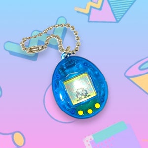 May include: A blue handheld digital pet game with a silver chain. The game has a small screen displaying a pixelated character and three yellow buttons below. The device is a nostalgic toy, popular in the 1990s.