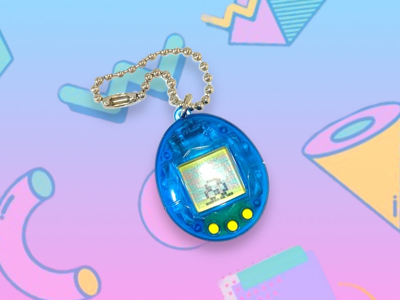 May include: A blue handheld digital pet game with a silver chain. The game has a small screen displaying a pixelated character and three yellow buttons below. The device is a nostalgic toy, popular in the 1990s.
