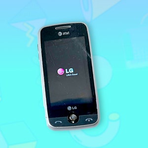 Może przedstawiać: Czarny telefon komórkowy LG z logo AT&T u góry. Ekran wyświetla logo LG ze słowami "Life's Good". Telefon ma srebrną obwódkę i mały przycisk na dole.