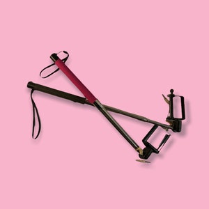 May include: Two selfie sticks, one black and one silver, with black phone holders. The black stick has a black handle and wrist strap. The silver stick has a red handle and wrist strap. A small audio jack is visible.