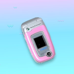 May include: A pink Sony Ericsson clamshell cell phone with a silver frame. The phone has a small screen and a camera. The background is a gradient of blue and pink with small wave shapes.