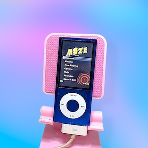 May include: A blue iPod music player with the word "MAZE" on the screen, held in a pink stand. The screen displays a menu with options like "Resume" and "Now Playing." The stand and the iPod are set against a gradient background.