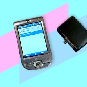 Puede incluir: Un PDA HP iPAQ plateado con una pantalla que muestra opciones de mensajería, junto a una funda de cuero negra. La pantalla del PDA muestra opciones para seleccionar una cuenta y configurar una nueva cuenta de correo electrónico. El fondo es una división de rosa y azul claro.