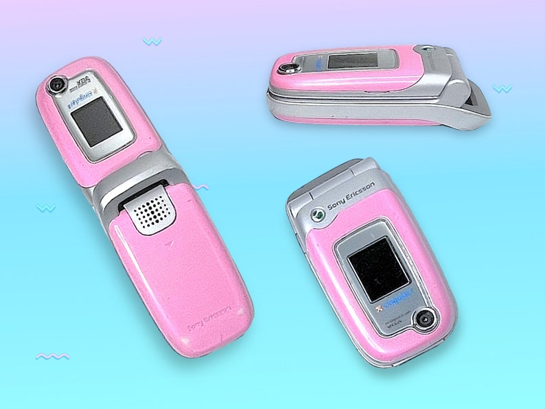 May include: Three pink Sony Ericsson flip phones are displayed against a gradient blue and purple background. The phones are open, closed, and at an angle, showcasing their silver accents, small screens, and camera lenses. The text "Sony Ericsson" is visible.