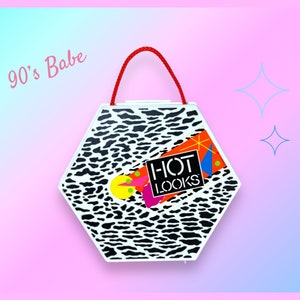 May include: A white, hexagonal handbag with a black and white animal print pattern. The bag features a red handle and a colorful graphic with the text "HOT LOOKS". The words "90's Babe" are written in pink on the upper left corner.