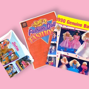 May include: Three vintage Barbie items are displayed against a pink background. The items include a 1990 Genuine Barbie catalog, a Fashion Doll Fashion booklet, and a Barbie package. The catalog features images of Barbie dolls in various outfits.