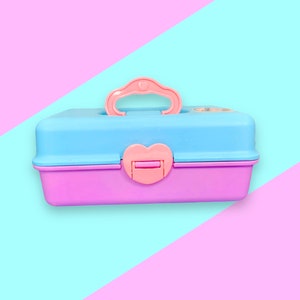 Puede incluir: Una caja de herramientas de plástico de dos tonos y colores pastel. La parte superior es azul claro, la inferior es rosa y el asa y el cierre son de color rosa a juego. El cierre tiene forma de corazón.