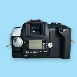 Pode incluir: C&acirc;mera de filme preta e prateada com visor digital e v&aacute;rios mostradores de controle. A c&acirc;mera possui um visor, uma sapata de flash e uma fixa&ccedil;&atilde;o para al&ccedil;a. A c&acirc;mera est&aacute; em um fundo azul claro.