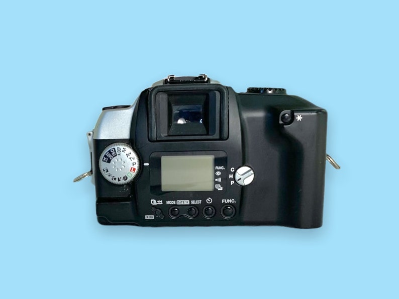 Pode incluir: C&acirc;mera de filme preta e prateada com visor digital e v&aacute;rios mostradores de controle. A c&acirc;mera possui um visor, uma sapata de flash e uma fixa&ccedil;&atilde;o para al&ccedil;a. A c&acirc;mera est&aacute; em um fundo azul claro.