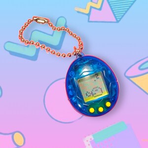 May include: A blue and red handheld virtual pet toy with a small screen displaying pixelated graphics. It has three yellow buttons and a gold-colored chain. The toy is a nostalgic item from the 90s.