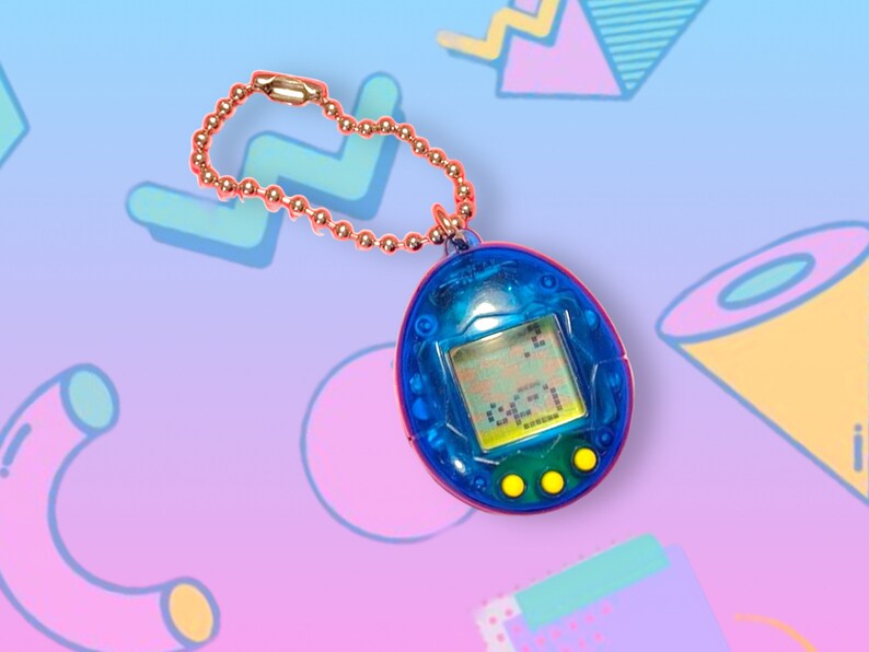 May include: A blue and red handheld virtual pet toy with a small screen displaying pixelated graphics. It has three yellow buttons and a gold-colored chain. The toy is a nostalgic item from the 90s.