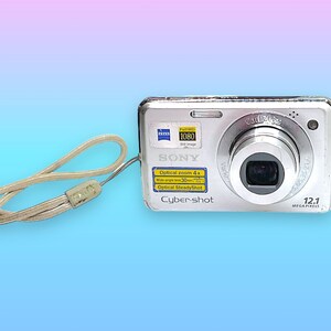 May include: Silver Sony Cyber-shot digital camera with a Carl Zeiss lens and a 12.1 megapixel resolution. Features include optical zoom and optical steady shot. Includes a beige wrist strap.