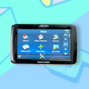 May include: A black Magellan RoadMate GPS device with a touch screen displaying a menu with options for address, points of interest, address book, intersection, previous, and city center. The screen has a blue background with white icons.