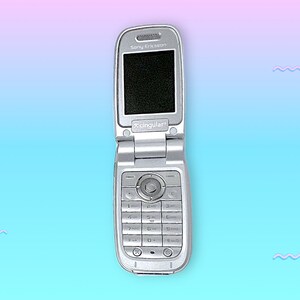 May include: Silver Sony Ericsson flip phone, open to reveal a black screen. The phone has a keypad and a circular navigation button. The Cingular logo is visible. The background is a gradient of pink and blue.