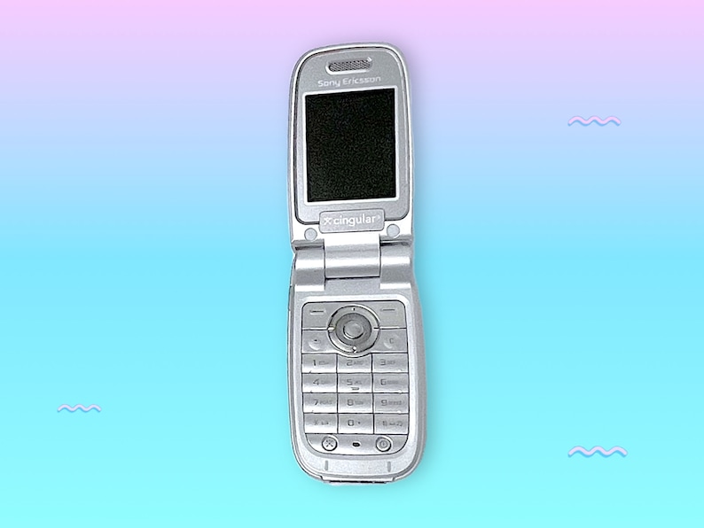 May include: Silver Sony Ericsson flip phone, open to reveal a black screen. The phone has a keypad and a circular navigation button. The Cingular logo is visible. The background is a gradient of pink and blue.