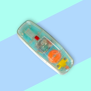 K&ouml;nnte beinhalten: Vintage Telefonh&ouml;rer aus klarem Kunststoff mit sichtbaren internen Komponenten. Der H&ouml;rer hat einen roten Knopf, einen orangefarbenen Lautsprecher und gelbe und blaue Akzente. Der Hintergrund ist hellblau und t&uuml;rkis.