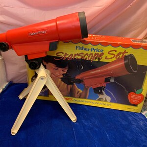 May include: A vintage Fisher-Price Starscope Set, featuring a red telescope with a black eyepiece and a cream-colored tripod. The box shows a child using the telescope. The set is designed for children.
