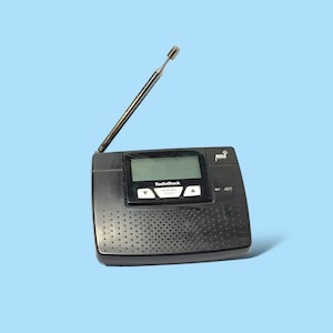 May include: A black RadioShack weather alert radio with a telescoping antenna. The radio has a small LCD screen and a speaker grill. The text "RadioShack" and "WEATHER ALERT" are visible on the front.