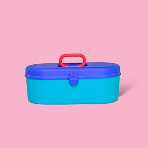 Puede incluir: Una caja de herramientas ovalada y colorida con asa roja, tapa azul y base turquesa. La caja de herramientas tiene un cierre de cierre y está sobre un fondo rosa. El asa está arqueada para facilitar el transporte.