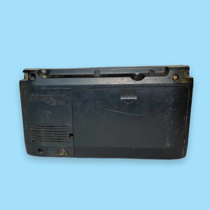 Może przedstawiać: Czarny boombox Sony CFS-W300S, widok z tyłu, na jasnoniebieskim tle. Boombox ma prostokątny kształt z uchwytem na g&oacute;rze i kratką głośnika po lewej stronie. Numer modelu i inne szczeg&oacute;ły są wydrukowane z tyłu.