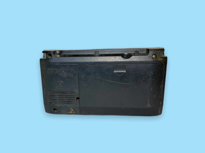 Może przedstawiać: Czarny boombox Sony CFS-W300S, widok z tyłu, na jasnoniebieskim tle. Boombox ma prostokątny kształt z uchwytem na g&oacute;rze i kratką głośnika po lewej stronie. Numer modelu i inne szczeg&oacute;ły są wydrukowane z tyłu.