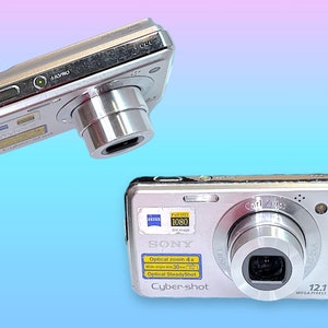 May include: Two silver Sony Cyber-shot digital cameras are displayed against a gradient blue and pink background. The cameras feature a Carl Zeiss lens, 12.1 megapixels, and optical zoom. One camera is positioned at an angle, while the other is facing forward.