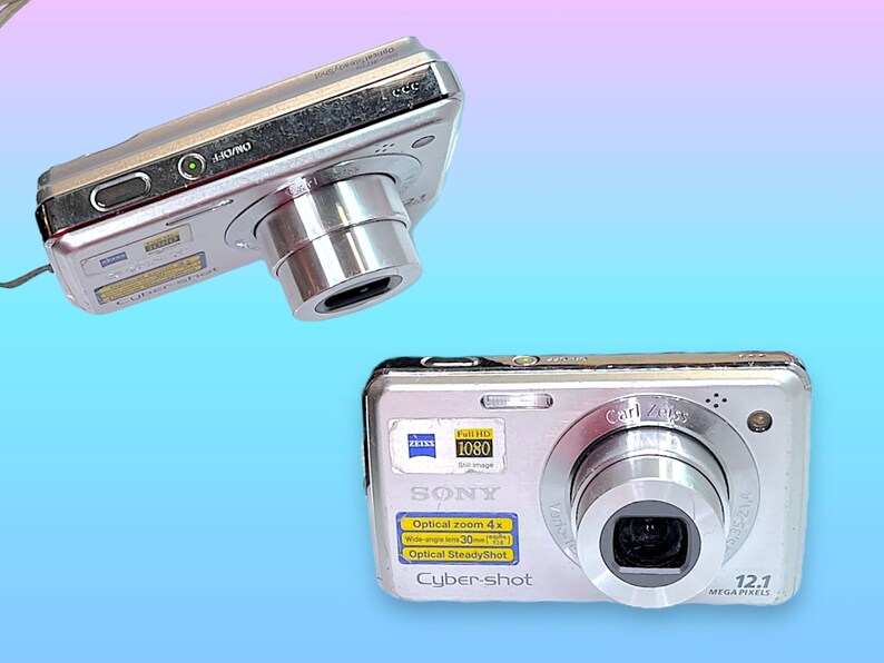 May include: Two silver Sony Cyber-shot digital cameras are displayed against a gradient blue and pink background. The cameras feature a Carl Zeiss lens, 12.1 megapixels, and optical zoom. One camera is positioned at an angle, while the other is facing forward.