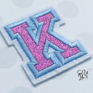 May include: A pink glitter letter K with a light blue outline. The letter is on a white background.