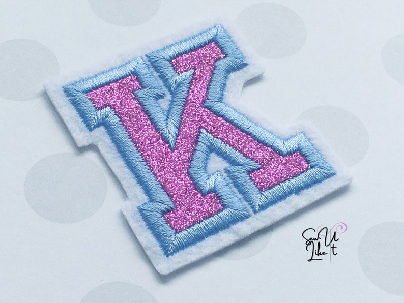 May include: A pink glitter letter K with a light blue outline. The letter is on a white background.