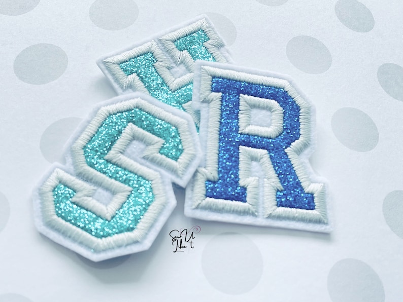 May include: Three felt letter patches in blue and turquoise with white stitching. The letters are "S", "R", and "T".