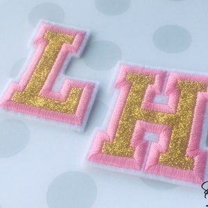 May include: Two felt letters, L and H, with pink outlines and gold glitter inside. The letters are on a white background with pink polka dots.