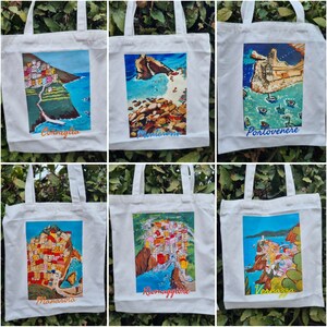 May include: Six white canvas tote bags with colourful images of Italian towns and cities. The bags feature the names of the towns: Corniglia, Manarola, Riomaggiore, Vernazza, Portovenere, and Monterosso.