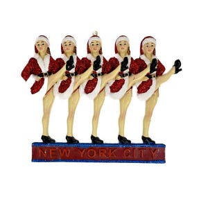 May include: Five red and white Santa Claus-themed dancers with glittery accents and black shoes, kicking their legs up in the air. The dancers are standing on a red and blue base with the text "NEW YORK CITY" in red.