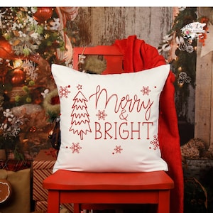 May include: White cushion with red embroidered text that says "Merry & Bright" with a stylised Christmas tree and snowflakes.
