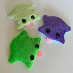 Peut inclure: Trois peluches aux tons verts et violets, chacune avec des yeux en boutons noirs et une langue rose. Les jouets ont une forme unique et abstraite, et sont faits d'une matière douce et duveteuse. Les jouets sont conçus pour être mignons et câlins.