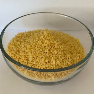 May include: A glass bowl filled with yellow couscous, a type of pasta made from semolina.