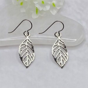 May include: Silver leaf dangle earrings with a delicate, intricate design. The earrings are on a white background.
