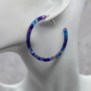 May include: A pair of blue and purple hoop earrings with a marbled pattern.