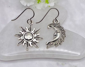 Könnte beinhalten: Ein Paar silberne Ohrringe mit einem Sonnen- und Mondmotiv. Die Sonne hat ein detailliertes Design mit Strahlen und der Mond hat ein Gesicht.