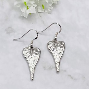 May include: A pair of silver dangle earrings with a hammered heart design. The hearts are pointed at the bottom and have a textured surface.
