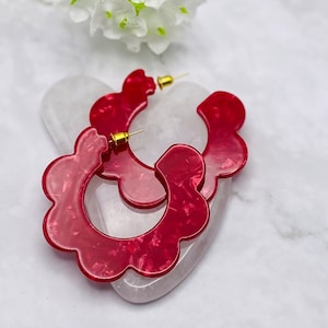 May include: A pair of red flower-shaped hoop earrings with a gold post.
