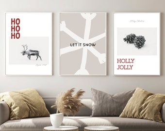 May include: Three minimalist Christmas-themed prints with white frames. The left print features a reindeer in a snowy landscape with the text "HO HO HO". The center print has a white snowflake design on a beige background with the text "LET IT SNOW". The right print features two pine cones on a white background with the text "HOLLY JOLLY".