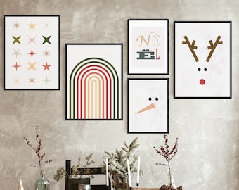 May include: Five framed prints on a wall with a table in front of them. The prints are all different designs. The first print is a white background with green and red stars. The second print is a rainbow arch with red, green, yellow, and orange stripes. The third print is a white background with the word "NOEL" in black letters. The fourth print is a white background with a snowman face. The fifth print is a white background with a red-nosed reindeer face. The table is covered with a white tablecloth and has a vase with red berries, a vase with a green plant, two candles, and a pine cone.