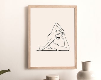 Op de afbeelding: Een zwart-witte lijntekening van een persoon in een yogapose, ingelijst in een licht houten lijst. De print is op een witte achtergrond en wordt getoond op een tafel met een vaas en een klein bakje.