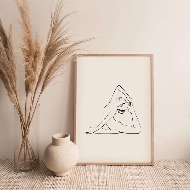 May include: A black and white line drawing of a person in a yoga pose, printed on a white background and framed in a light wood frame.