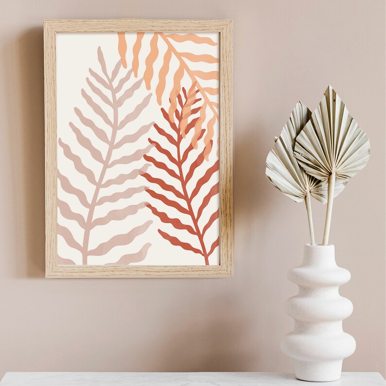 May include: A framed print with a minimalist design featuring three stylized fern leaves in shades of pink, orange, and red on a white background.