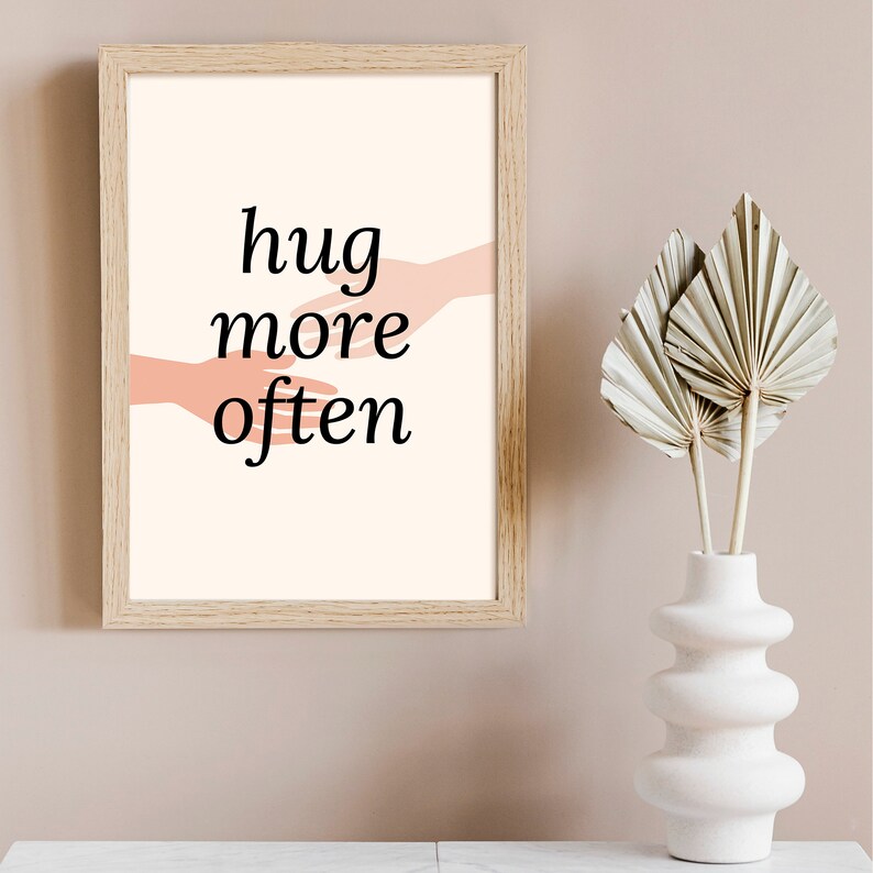 Puede incluir: Una impresi&oacute;n enmarcada con fondo blanco y el texto "hug more often" en negro. Dos manos rosas se acercan la una a la otra en el centro de la impresi&oacute;n.