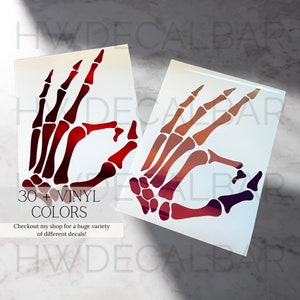 May include: Two skeleton hand decals in an OK sign gesture. The decals are printed on a white background and have a gradient of red, orange, and purple colors. The text "30+ VINYL COLORS" and "Checkout my shop for a huge variety of different decals!" is printed below the decals.