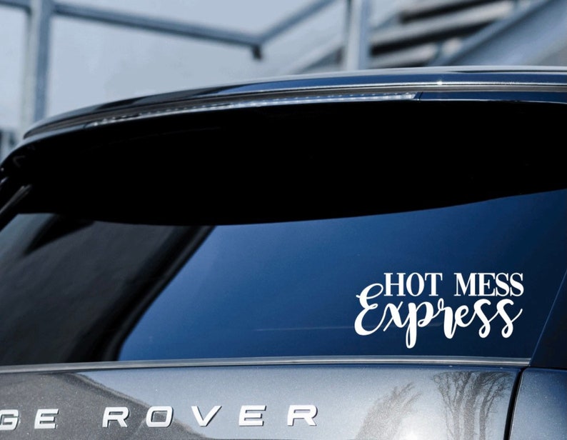 May include: A white vinyl decal with the text "HOT MESS Express" in a cursive font, applied to the rear window of a silver car.